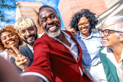 Mennesker af forskellig alder, race og køn smiler bredt uden for en bygning